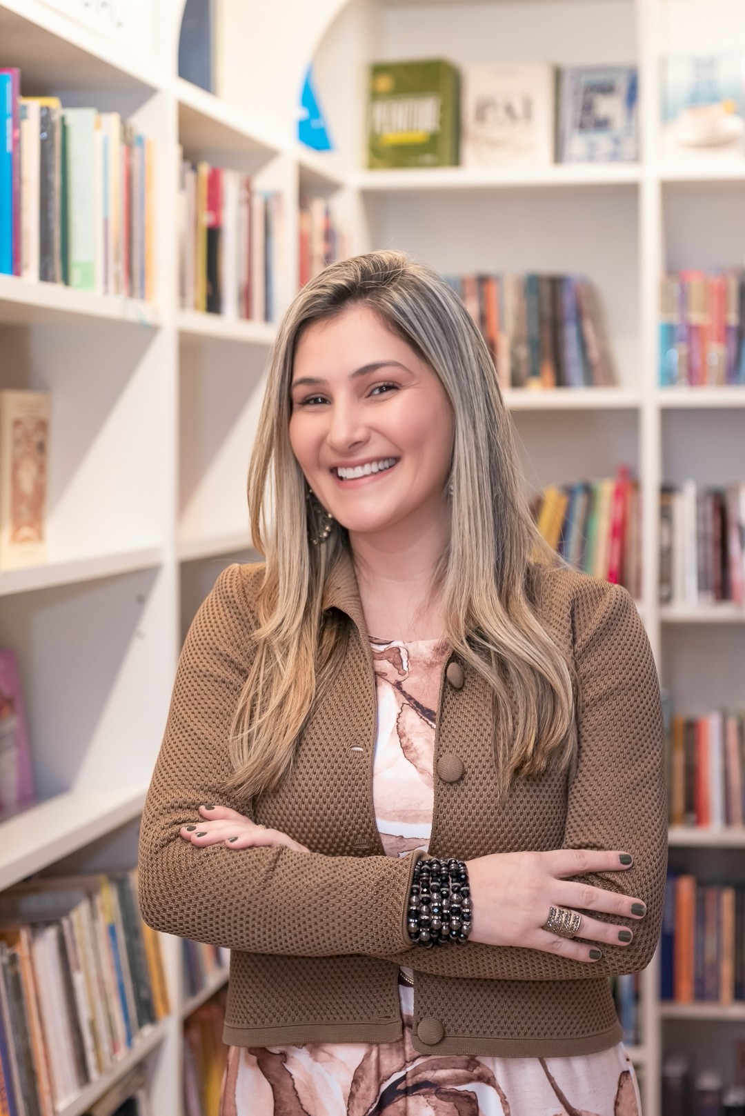 Juliana Cava Tanaka sorrindo em frente a uma estante de livros